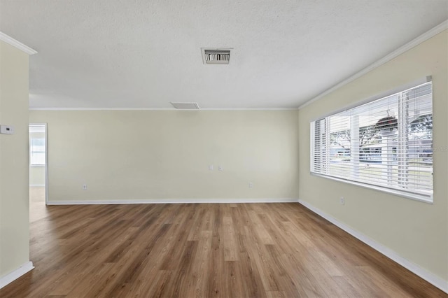 empty room with a textured ceiling, hardwood / wood-style flooring, and crown molding