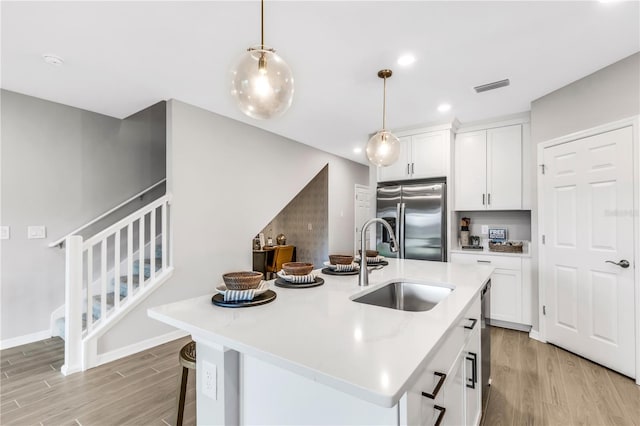 kitchen with pendant lighting, a kitchen island with sink, sink, stainless steel refrigerator with ice dispenser, and light hardwood / wood-style floors