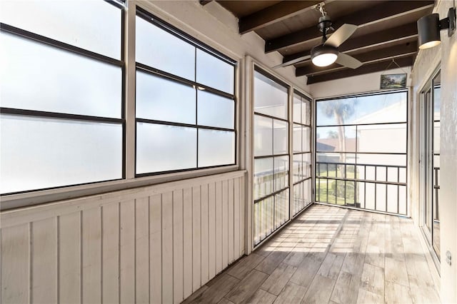 unfurnished sunroom featuring beamed ceiling, plenty of natural light, and ceiling fan