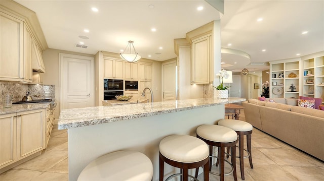 kitchen featuring tasteful backsplash, light stone counters, cream cabinets, hanging light fixtures, and a breakfast bar area