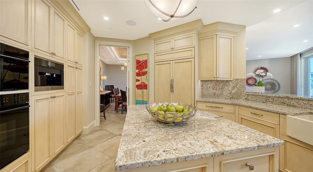 kitchen with cream cabinetry, black oven, paneled built in refrigerator, and light stone countertops