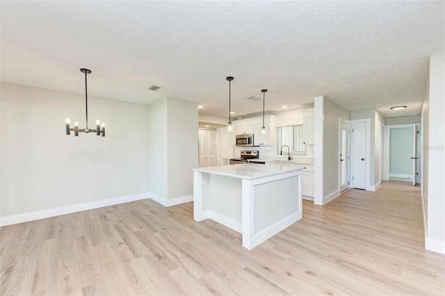 kitchen featuring appliances with stainless steel finishes, white cabinets, a center island, light hardwood / wood-style floors, and hanging light fixtures