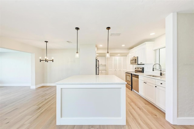 kitchen featuring appliances with stainless steel finishes, sink, decorative light fixtures, white cabinets, and a kitchen island