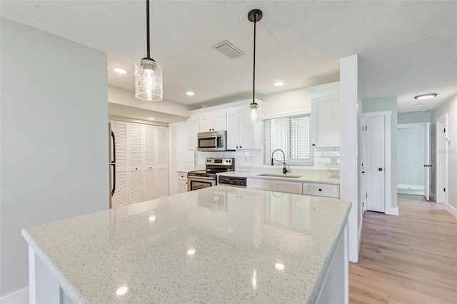 kitchen with appliances with stainless steel finishes, light stone counters, sink, white cabinets, and hanging light fixtures