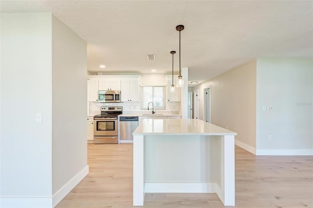 kitchen featuring sink, decorative light fixtures, light hardwood / wood-style floors, white cabinetry, and stainless steel appliances