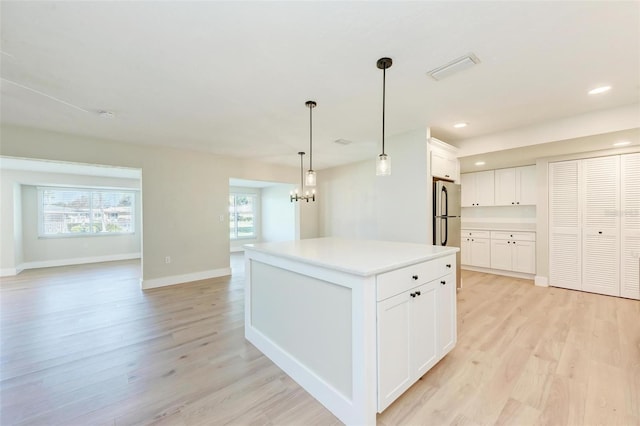 kitchen with a kitchen island, light hardwood / wood-style flooring, white cabinetry, hanging light fixtures, and stainless steel refrigerator