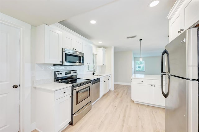 kitchen with white cabinets, hanging light fixtures, sink, appliances with stainless steel finishes, and light hardwood / wood-style floors