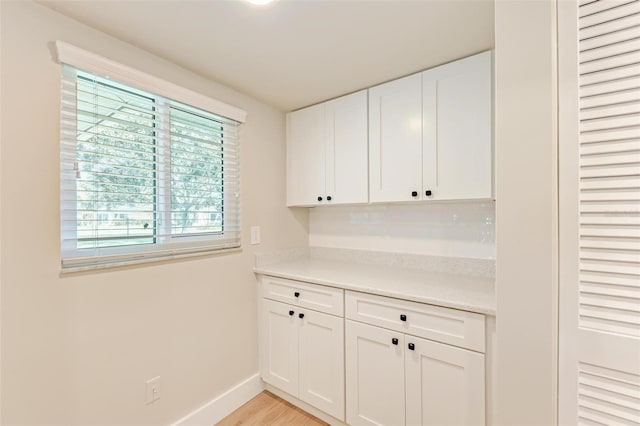 interior space with tasteful backsplash, white cabinets, and light wood-type flooring