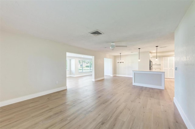 unfurnished living room with ceiling fan with notable chandelier and light wood-type flooring