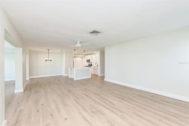 unfurnished living room featuring ceiling fan with notable chandelier and light hardwood / wood-style floors