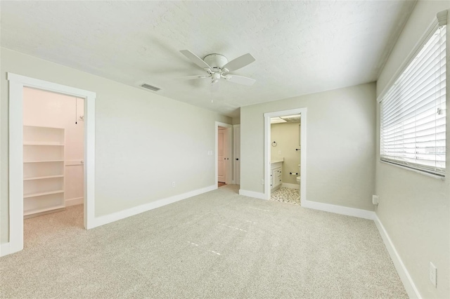 unfurnished bedroom featuring light carpet, a walk in closet, ceiling fan, connected bathroom, and a closet