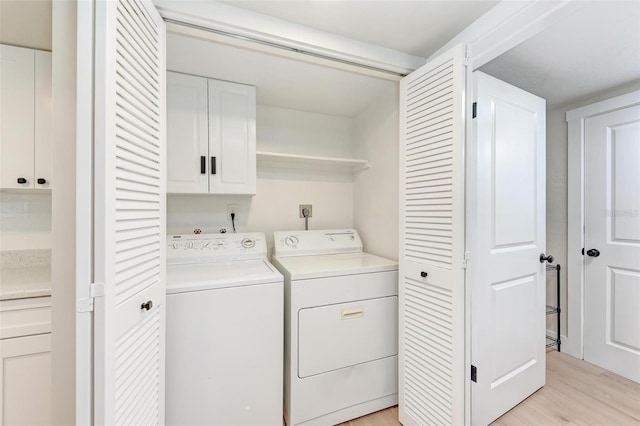 laundry area with washing machine and clothes dryer, cabinets, and light wood-type flooring