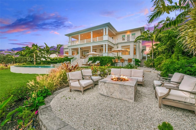 back house at dusk featuring a balcony, an outdoor living space with a fire pit, and a patio