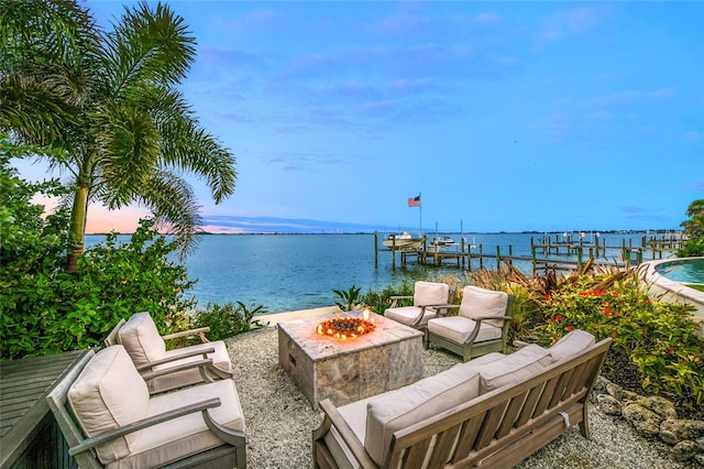 patio terrace at dusk with a water view, an outdoor fire pit, and a dock