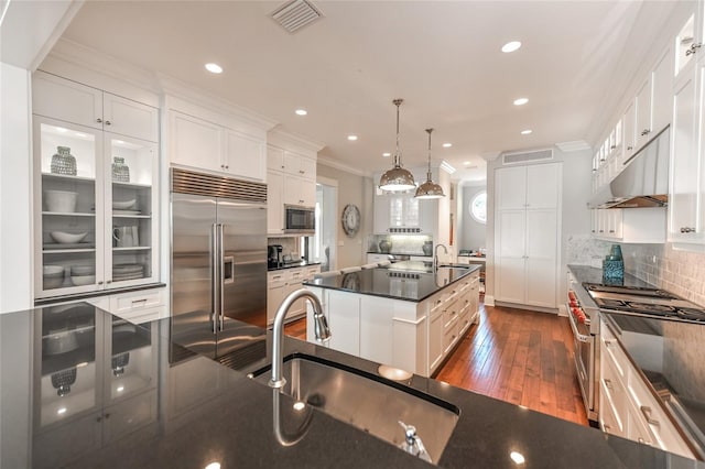 kitchen featuring a center island with sink, sink, hanging light fixtures, built in appliances, and dark hardwood / wood-style floors