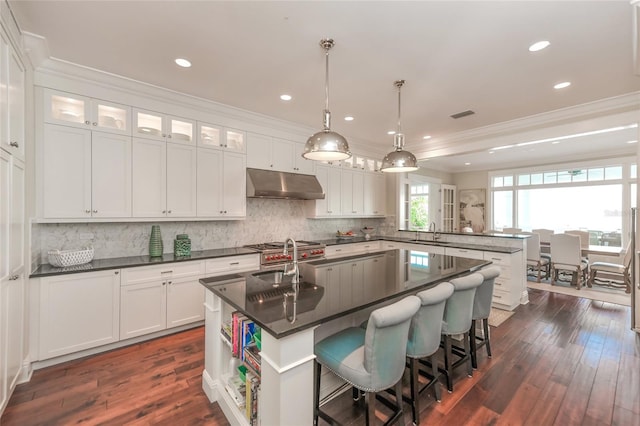 kitchen with dark wood-type flooring, a center island with sink, white cabinets, sink, and hanging light fixtures