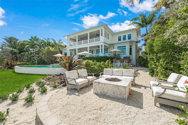 rear view of house with ceiling fan, a balcony, a patio, and an outdoor living space with a fire pit