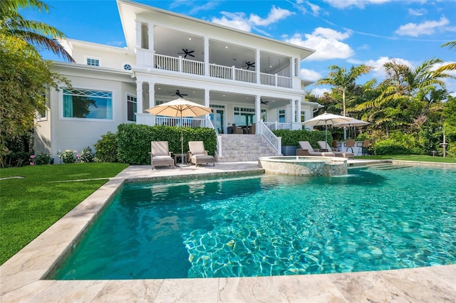 rear view of house with ceiling fan, a swimming pool with hot tub, a balcony, and a patio