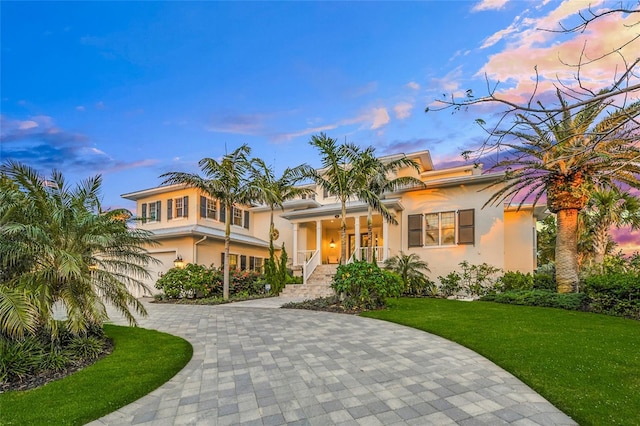 mediterranean / spanish house featuring covered porch, a garage, and a lawn