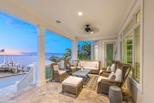 patio terrace at dusk featuring outdoor lounge area, a boat dock, a water view, and ceiling fan