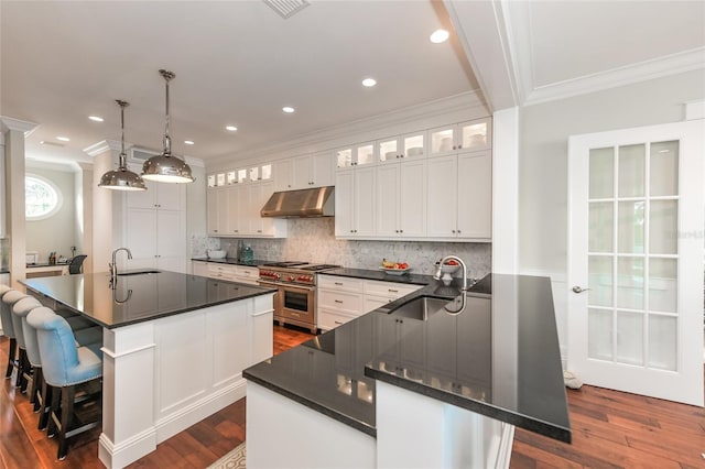 kitchen with hanging light fixtures, white cabinets, a kitchen island with sink, and sink