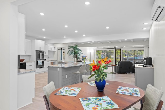 dining space with beamed ceiling, light wood-type flooring, and a wall unit AC