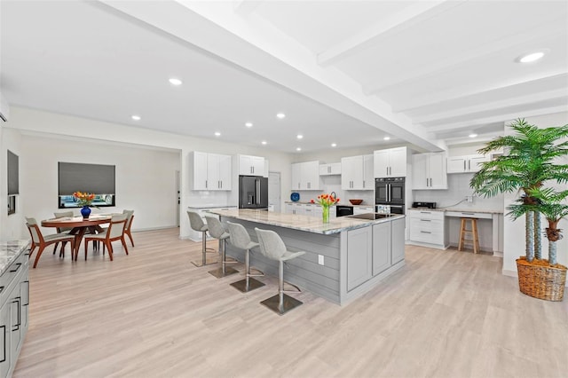 kitchen featuring a large island, light stone countertops, high end fridge, white cabinets, and light wood-type flooring