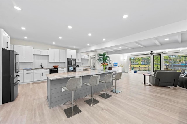 kitchen with black appliances, a kitchen breakfast bar, a large island, light stone counters, and white cabinetry