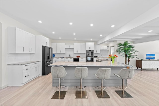 kitchen with white cabinetry, light stone countertops, light hardwood / wood-style flooring, a large island with sink, and appliances with stainless steel finishes