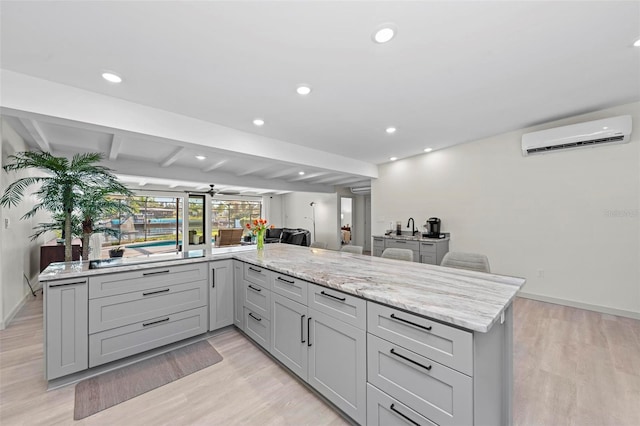 kitchen with light hardwood / wood-style floors, light stone counters, an AC wall unit, and beam ceiling