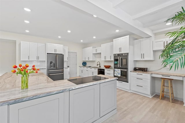 kitchen featuring high quality fridge, black electric stovetop, multiple ovens, light wood-type flooring, and white cabinetry