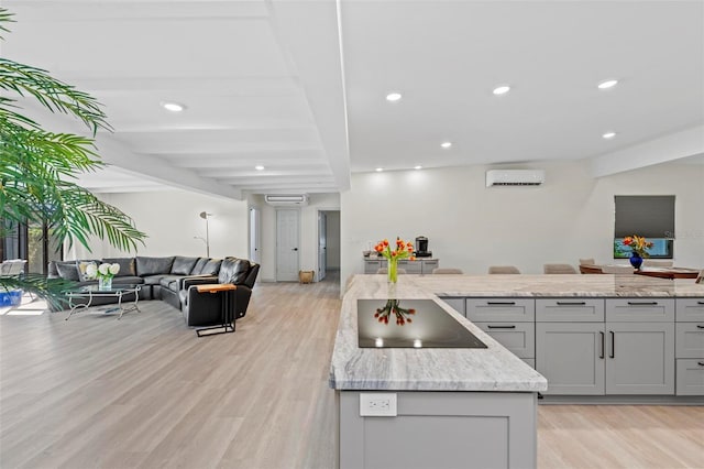 kitchen with a wall mounted air conditioner, gray cabinets, light stone counters, and light wood-type flooring