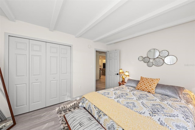 bedroom with light wood-style floors, a closet, and beamed ceiling