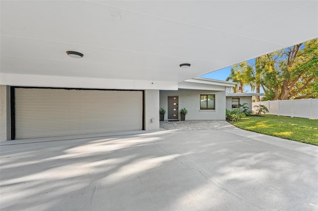 view of front of home with stucco siding, a front yard, fence, a garage, and driveway