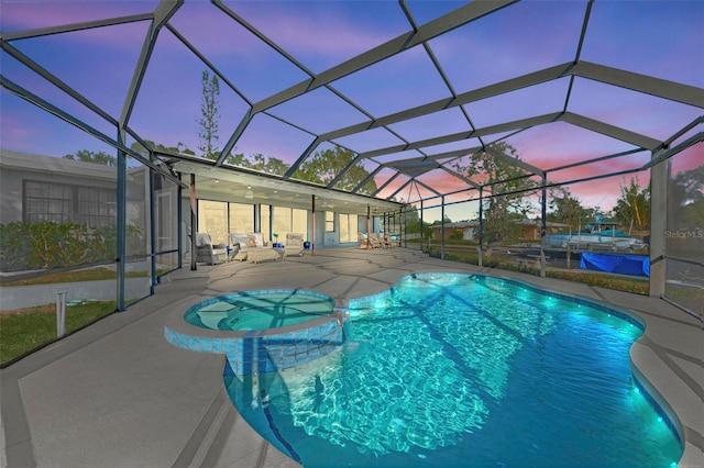 pool at dusk featuring a patio, a lanai, and a pool with connected hot tub