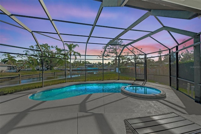 pool at dusk featuring glass enclosure, a patio, a water view, and a pool with connected hot tub