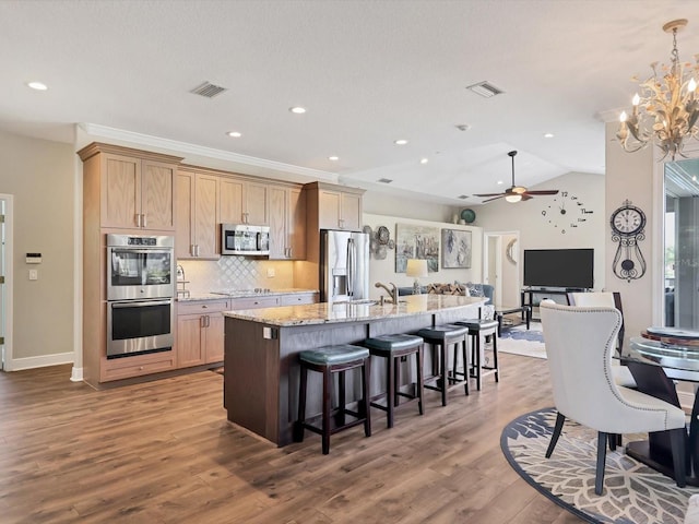 kitchen featuring ceiling fan with notable chandelier, vaulted ceiling, hardwood / wood-style flooring, an island with sink, and stainless steel appliances