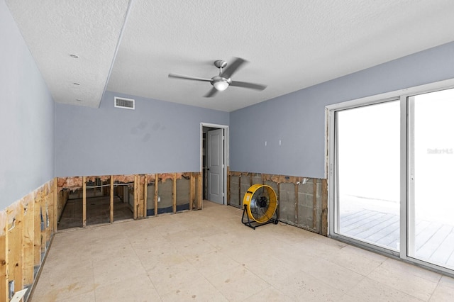 empty room featuring a textured ceiling, ceiling fan, and tile walls