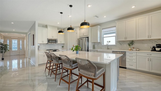 kitchen with appliances with stainless steel finishes, a center island, decorative light fixtures, and white cabinetry