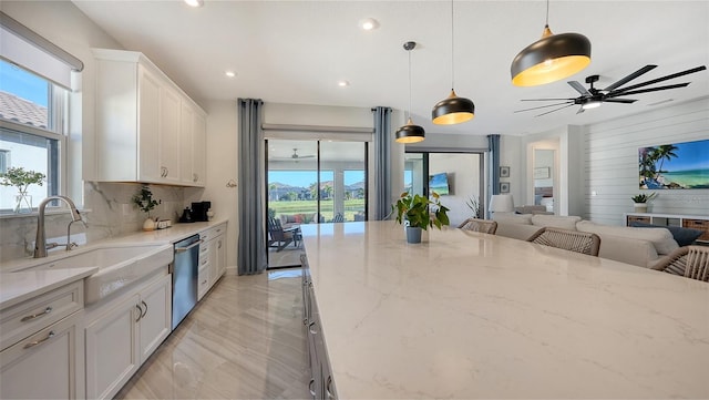 kitchen featuring white cabinets, sink, hanging light fixtures, light stone countertops, and tasteful backsplash