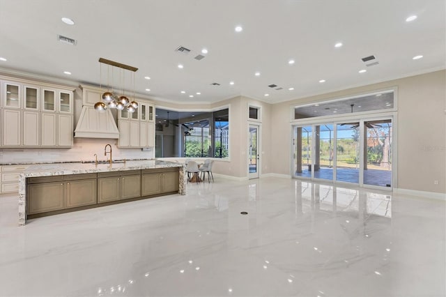 kitchen featuring a spacious island, light stone counters, crown molding, decorative light fixtures, and cream cabinets