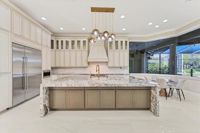 kitchen with pendant lighting, sink, a large island with sink, stainless steel built in fridge, and light stone countertops