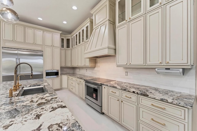 kitchen with stainless steel appliances, light stone countertops, sink, and cream cabinetry