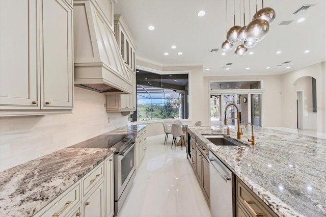 kitchen with premium range hood, decorative light fixtures, sink, stainless steel appliances, and cream cabinets