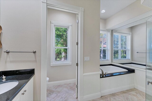 bathroom featuring vanity, plenty of natural light, a tub, and toilet