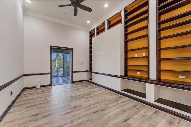 empty room featuring crown molding, ceiling fan, built in shelves, and light hardwood / wood-style floors