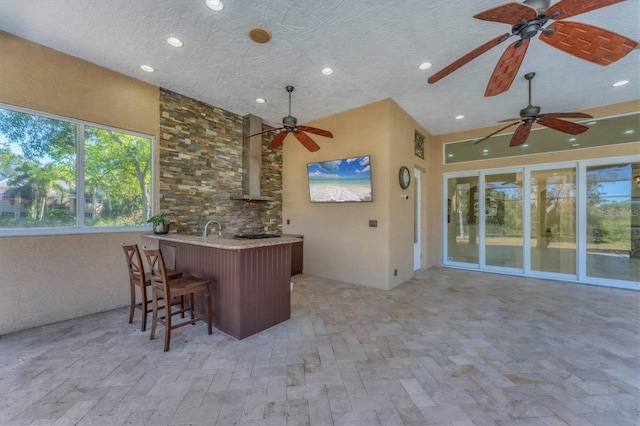 kitchen featuring a breakfast bar, sink, kitchen peninsula, wall chimney range hood, and a textured ceiling