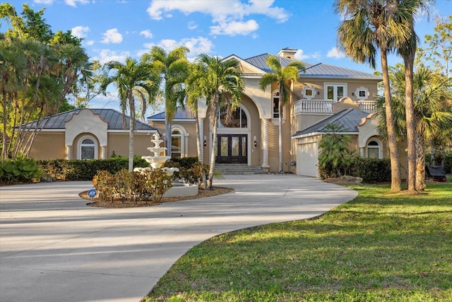 mediterranean / spanish house featuring metal roof, concrete driveway, french doors, stucco siding, and a standing seam roof