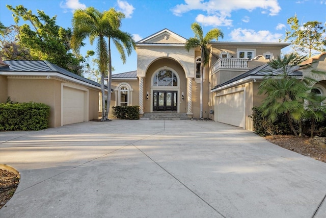 mediterranean / spanish-style house with concrete driveway, a balcony, a standing seam roof, french doors, and stucco siding