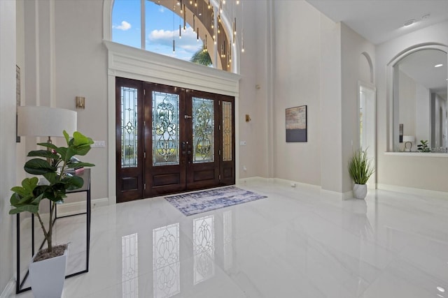 entrance foyer featuring marble finish floor, a towering ceiling, and baseboards